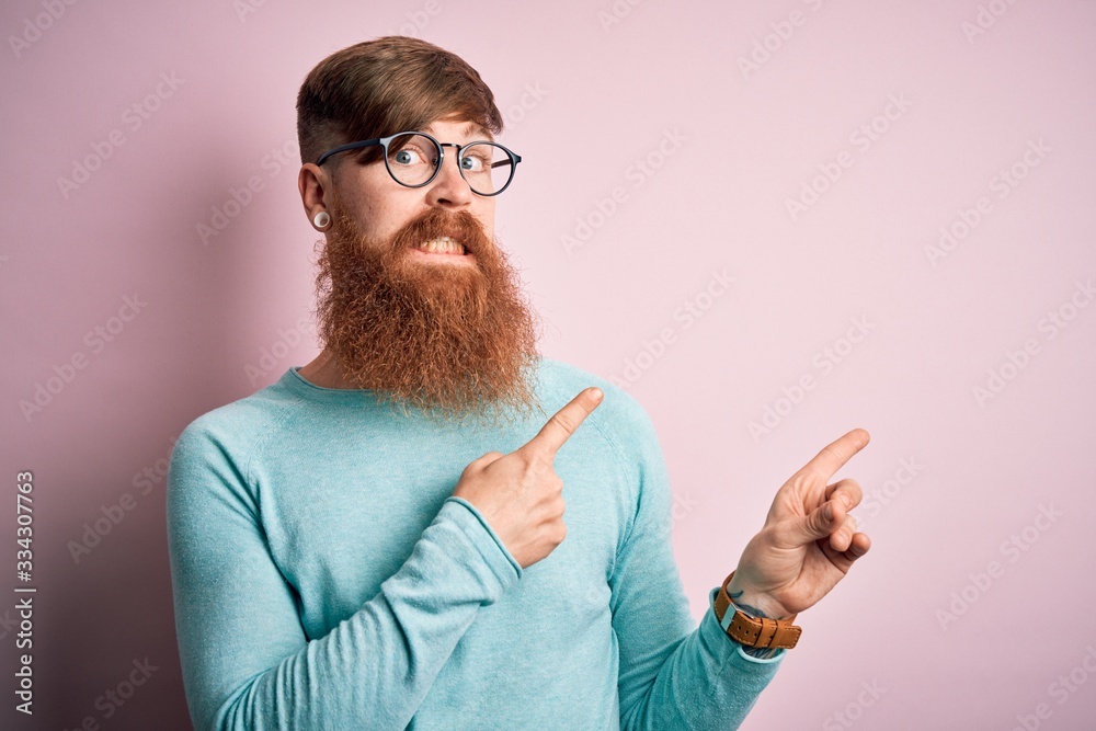 Handsome Irish redhead man with beard wearing glasses over pink isolated background Pointing aside worried and nervous with both hands, concerned and surprised expression Handsome Irish redhead man with beard wearing glasses over pink isolated background Pointing aside worried and nervous with both hands, concerned and surprised expression