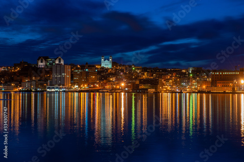 St. John's waterfront harbour at night during the blue hour. The lights on the water are bright yellow and orange which are reflecting from the skyline in the stillness of the smooth water. 