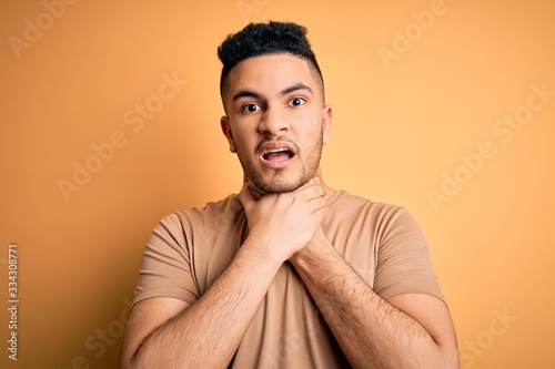Young handsome man wearing casual t-shirt standing over isolated yellow background shouting and suffocate because painful strangle. Health problem. Asphyxiate and suicide concept. © Krakenimages.com