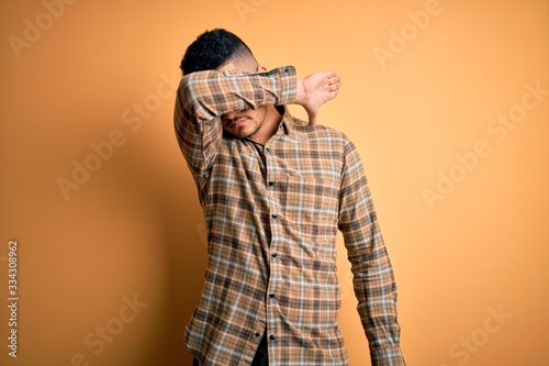 Young handsome man wearing casual shirt standing over isolated yellow background covering eyes with arm, looking serious and sad. Sightless, hiding and rejection concept