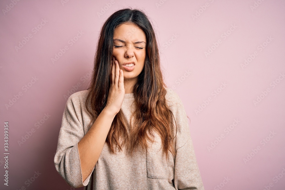 Young beautiful brunette woman wearing casual sweater standing over pink background touching mouth with hand with painful expression because of toothache or dental illness on teeth. Dentist Young beautiful brunette woman wearing casual sweater standing over pink background touching mouth with hand with painful expression because of toothache or dental illness on teeth. Dentist