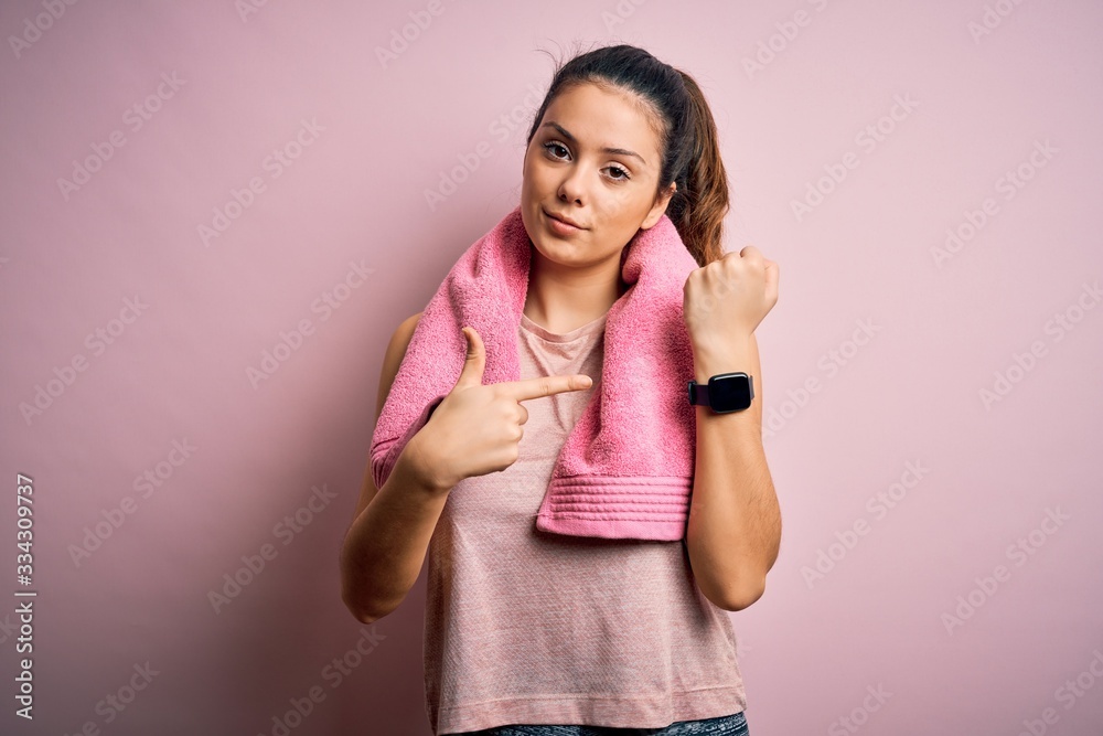 Young beautiful brunette sportswoman wearing sportswear and towel over pink background In hurry pointing to watch time, impatience, looking at the camera with relaxed expression Young beautiful brunette sportswoman wearing sportswear and towel over pink background In hurry pointing to watch time, impatience, looking at the camera with relaxed expression