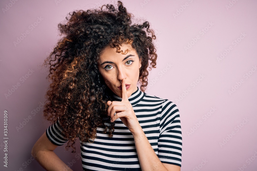 Young beautiful woman with curly hair and piercing wearing casual striped t-shirt asking to be quiet with finger on lips. Silence and secret concept. Young beautiful woman with curly hair and piercing wearing casual striped t-shirt asking to be quiet with finger on lips. Silence and secret concept.