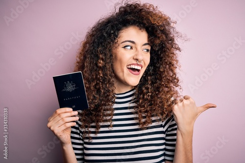 Beautiful tourist woman with curly hair and piercing holding australia australian passport id pointing and showing with thumb up to the side with happy face smiling