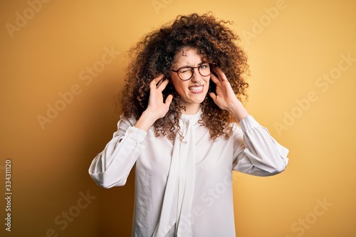 Young beautiful brunette woman with curly hair and piercing wearing shirt and glasses covering ears with fingers with annoyed expression for the noise of loud music. Deaf concept.