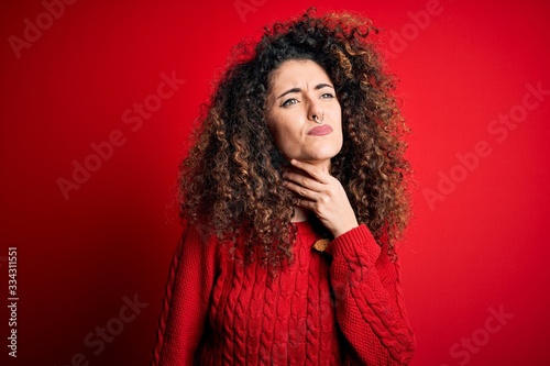 Young beautiful woman with curly hair and piercing wearing casual red sweater Touching painful neck  sore throat for flu  clod and infection