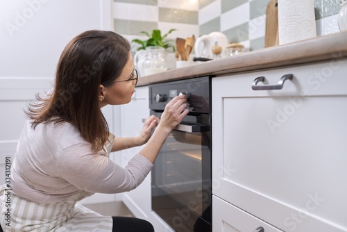 Mature woman in apron near the oven in the kitchen