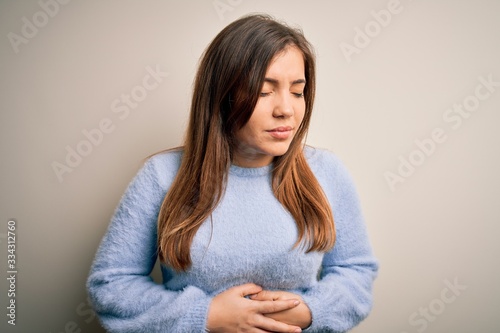 Beautiful young woman wearing casual winter sweater standing over isolated background with hand on stomach because indigestion, painful illness feeling unwell. Ache concept.