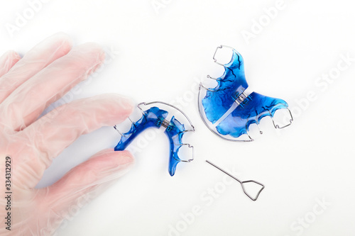 An orthodontist's hand with disposable gloves holds an orthodontic appliance for children on a white table in the dentist's office. Concept of oral health in childhood.