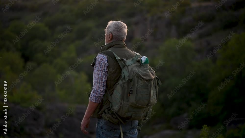 Back view senior bearded man with a backpack looking at a mountains and nature Back view senior bearded man with a backpack looking at a mountains and nature