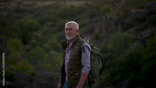 Senior man with gray hair, handsome tourist with backpack with a beard stay at the edge of the canyon and looking around. Senior man walking
