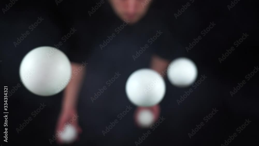 Circus artist wearing black juggling with white balls in slow motion