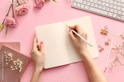 Woman writing something in notebook on color background