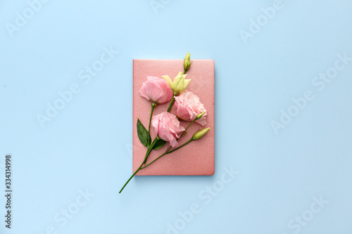 Notebook with eustoma flowers on color background
