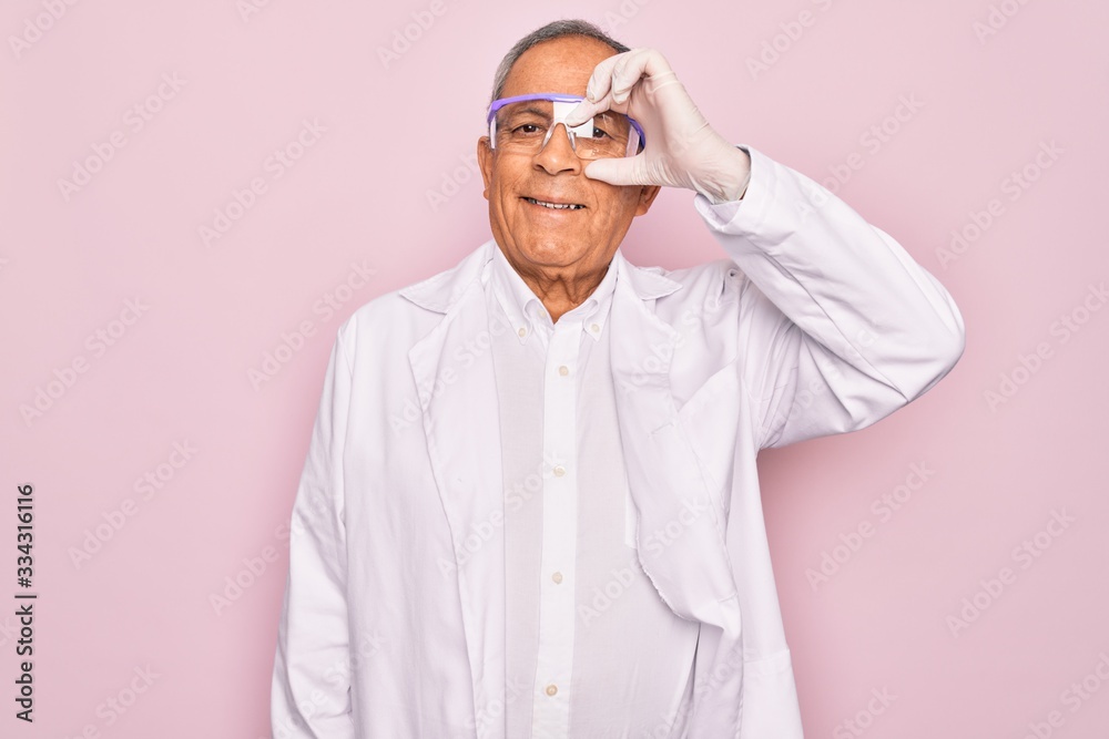 Fototapeta premium Senior grey-haired scientist man wearing glasses and coat over isolated pink background doing ok gesture with hand smiling, eye looking through fingers with happy face.