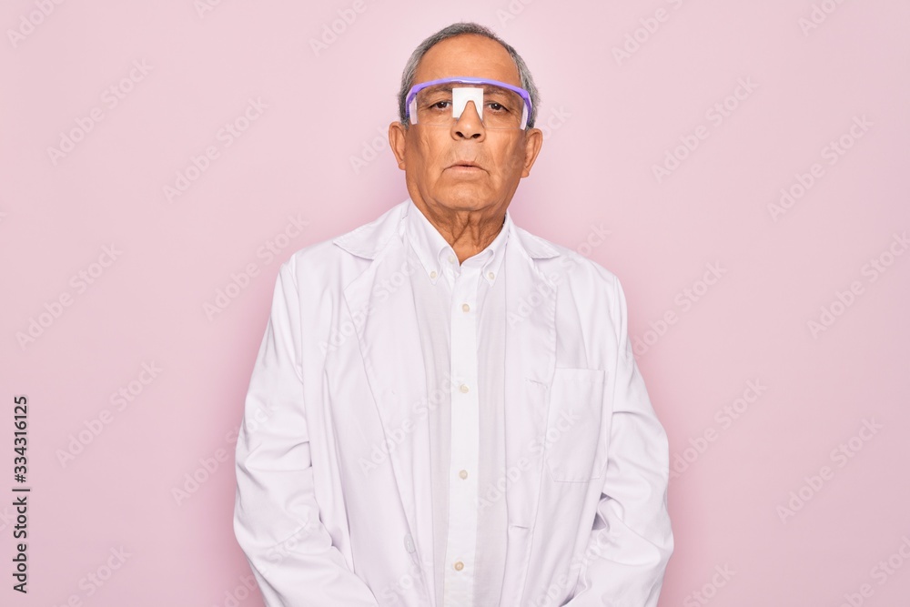 Senior grey-haired scientist man wearing glasses and coat over isolated pink background with serious expression on face. Simple and natural looking at the camera. Senior grey-haired scientist man wearing glasses and coat over isolated pink background with serious expression on face. Simple and natural looking at the camera.