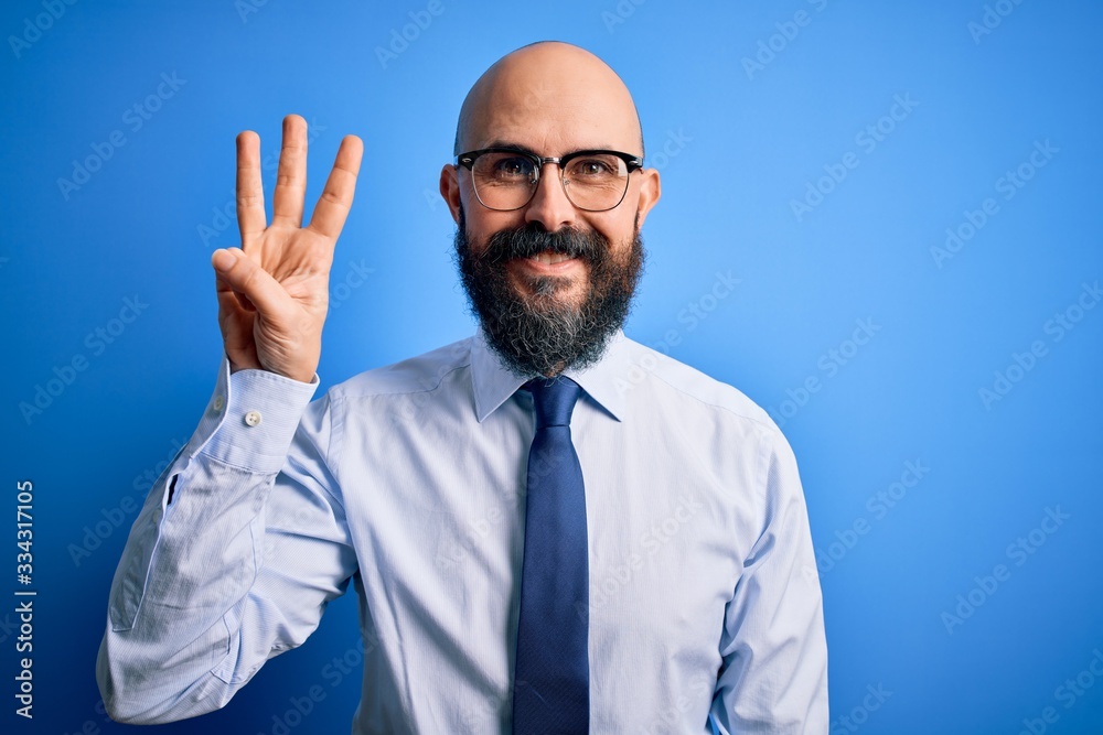 Handsome business bald man with beard wearing elegant tie and glasses over blue background showing and pointing up with fingers number three while smiling confident and happy. Handsome business bald man with beard wearing elegant tie and glasses over blue background showing and pointing up with fingers number three while smiling confident and happy.