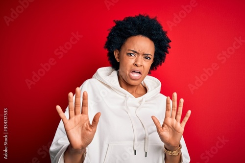 Young beautiful African American afro sportswoman with curly hair wearing sportswear disgusted expression, displeased and fearful doing disgust face because aversion reaction. With hands raised