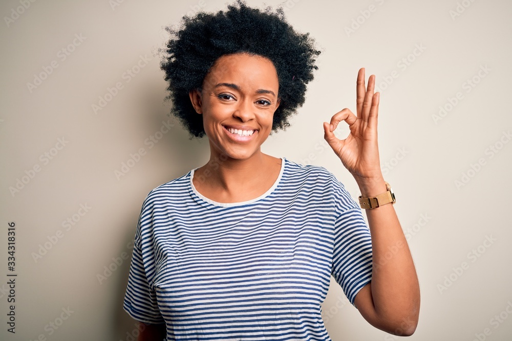 Young beautiful African American afro woman with curly hair wearing striped t-shirt smiling positive doing ok sign with hand and fingers. Successful expression. Young beautiful African American afro woman with curly hair wearing striped t-shirt smiling positive doing ok sign with hand and fingers. Successful expression.