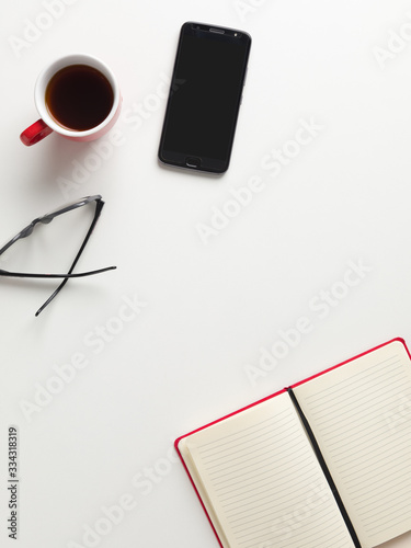 Top view workspace, a blank notebook, mobile, cup of coffee, glasses, white background with space for writing. Top view mockup smartphone black screen