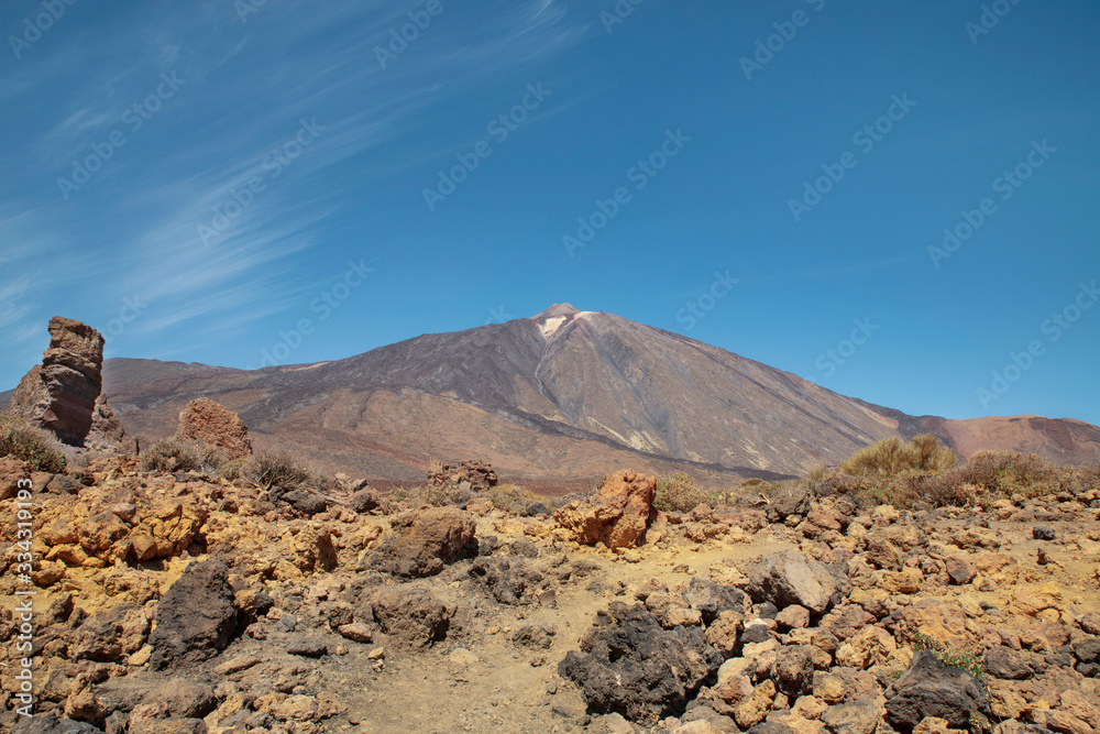 Mount Teide surrounded by the rocky volcanic and unusual landscape with Roque Cinchado on the left, situated in the popular travel destination Teide National Park, in Tenerife, Canary Islands, Spain