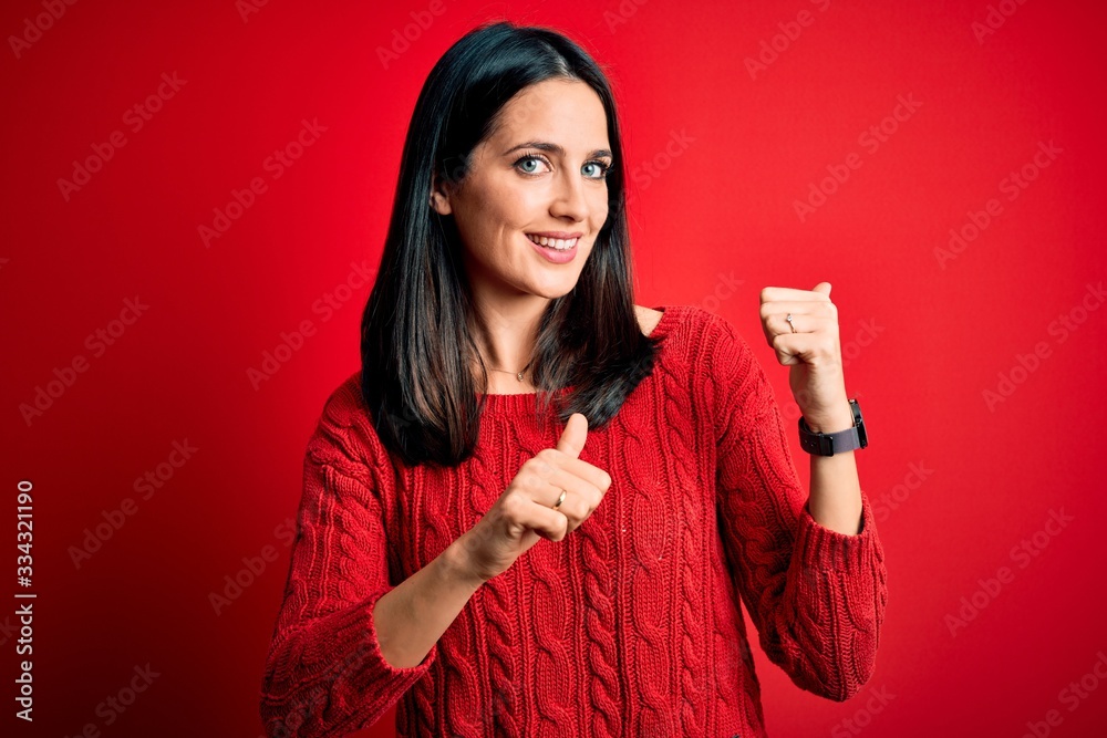 Young brunette woman with blue eyes wearing casual sweater over isolated red background Pointing to the back behind with hand and thumbs up, smiling confident Young brunette woman with blue eyes wearing casual sweater over isolated red background Pointing to the back behind with hand and thumbs up, smiling confident