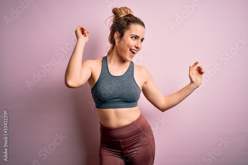Young beautiful blonde sportswoman doing sport wearing sportswear over pink background Dancing happy and cheerful, smiling moving casual and confident listening to music © Krakenimages.com