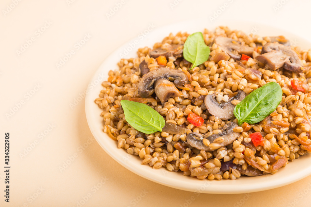 Spelt (dinkel wheat) porridge with vegetables and mushrooms on ceramic plate on orange background. Side view, close up. Spelt (dinkel wheat) porridge with vegetables and mushrooms on ceramic plate on orange background. Side view, close up.