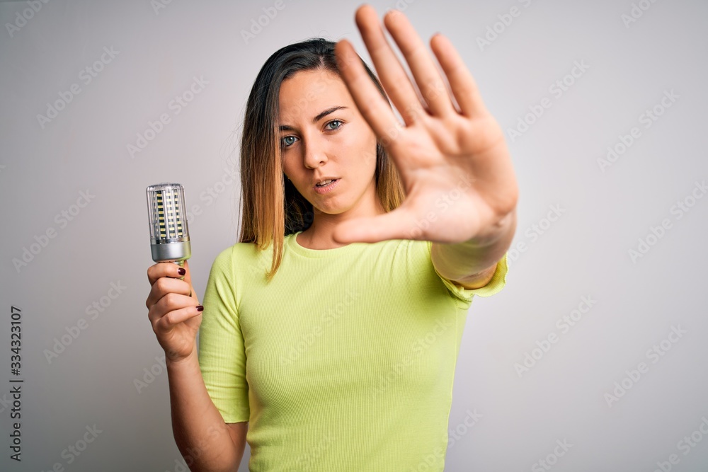 Young beautiful blonde woman holding led lightbulb over isolated white background with open hand doing stop sign with serious and confident expression, defense gesture Young beautiful blonde woman holding led lightbulb over isolated white background with open hand doing stop sign with serious and confident expression, defense gesture