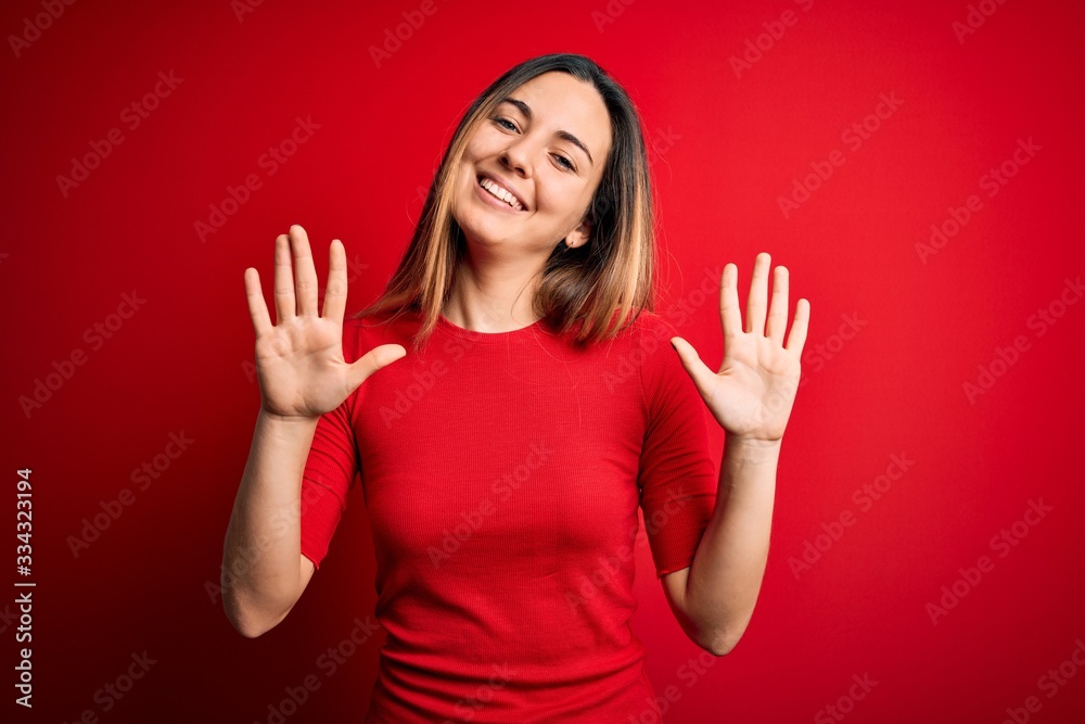 Young beautiful blonde woman with blue eyes wearing casual t-shirt over red background showing and pointing up with fingers number ten while smiling confident and happy. Young beautiful blonde woman with blue eyes wearing casual t-shirt over red background showing and pointing up with fingers number ten while smiling confident and happy.