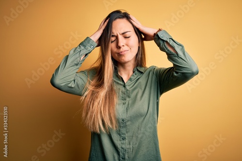 Young beautiful blonde woman with blue eyes wearing green shirt over yellow background suffering from headache desperate and stressed because pain and migraine. Hands on head. © Krakenimages.com