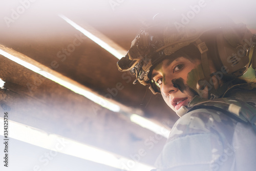 Konstfotografi Close up view through hole of wood wall of beautiful soldier woman with combat suit look to the camera