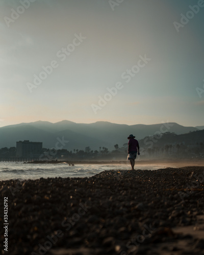 Women wearing hat walks along the beach searching for seashells