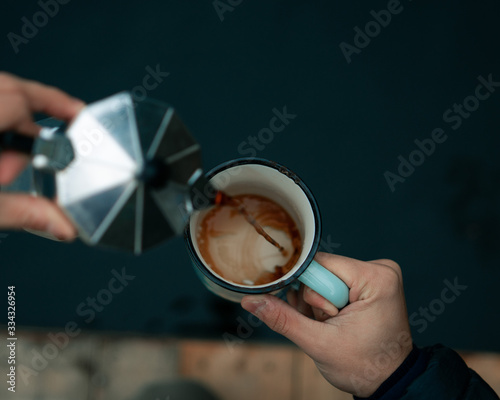 Young man pouring coffee in ceramic cup outdoors