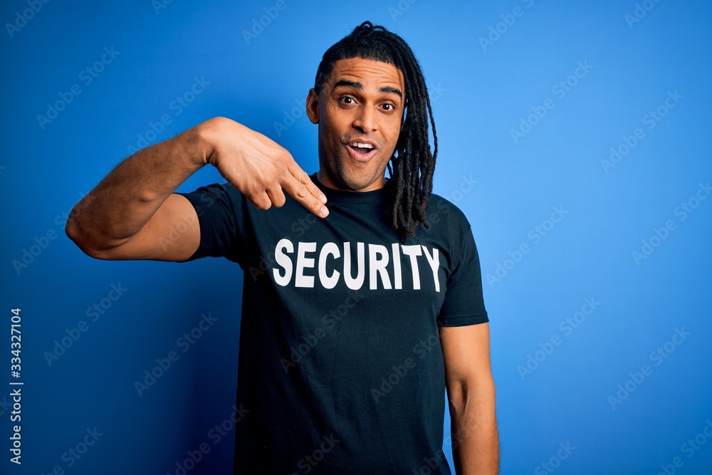 Young african american afro safeguard man with dreadlocks wearing security uniform with surprise face pointing finger to himself