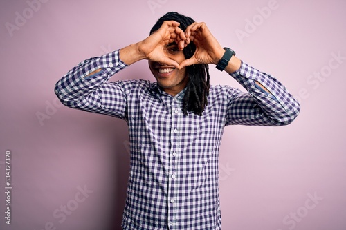 Young handsome african american afro man with dreadlocks wearing casual shirt Doing heart shape with hand and fingers smiling looking through sign
