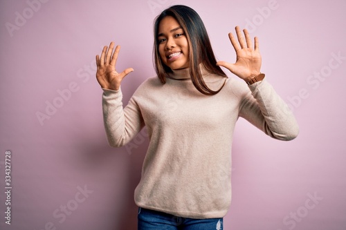 Young beautiful asian girl wearing casual turtleneck sweater over isolated pink background showing and pointing up with fingers number ten while smiling confident and happy.