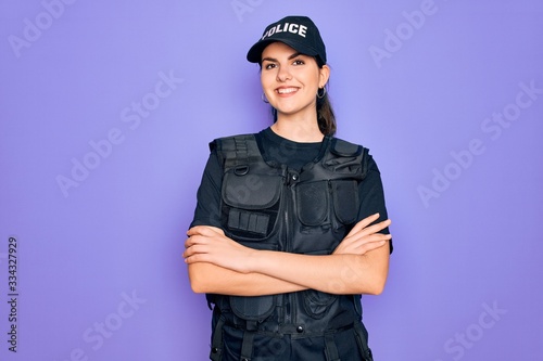 Fotografie Young police woman wearing security bulletproof vest uniform over purple background happy face smiling with crossed arms looking at the camera