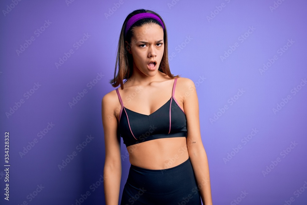 Obraz premium Young beautiful sporty girl doing sport wearing sportswear over isolated purple background In shock face, looking skeptical and sarcastic, surprised with open mouth