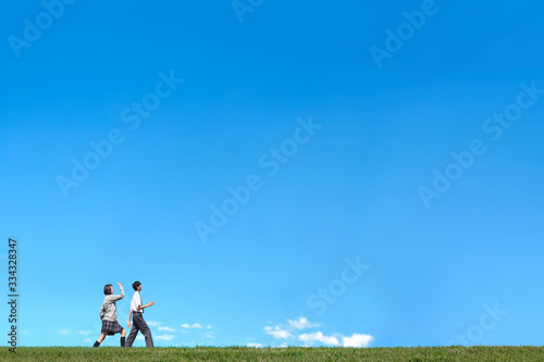 青空背景で男女2人が並んで歩く様子。進学,入学,進路イメージ