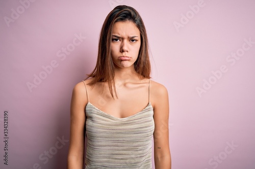 Young beautiful brunette girl wearing casual striped t-shirt over isolated pink background depressed and worry for distress, crying angry and afraid. Sad expression.