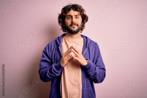 Young handsome sporty man with beard wearing casual sweatshirt over pink background Hands together and fingers crossed smiling relaxed and cheerful. Success and optimistic