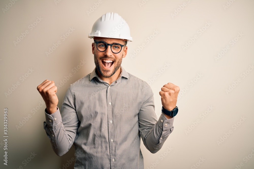 Young architect man wearing builder safety helmet over isolated background celebrating surprised and amazed for success with arms raised and open eyes. Winner concept.