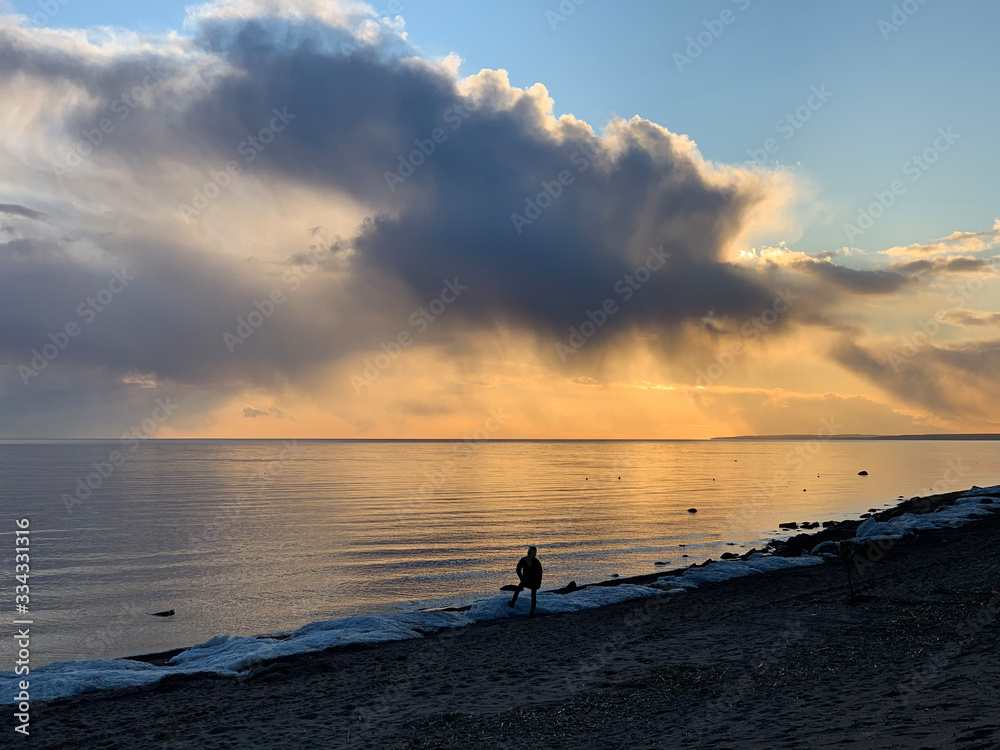 The coast at sunset, the picturesque sunset, quiet water, a sandy beach, clouds are illuminated by the sunset sun, Specular reflection in water