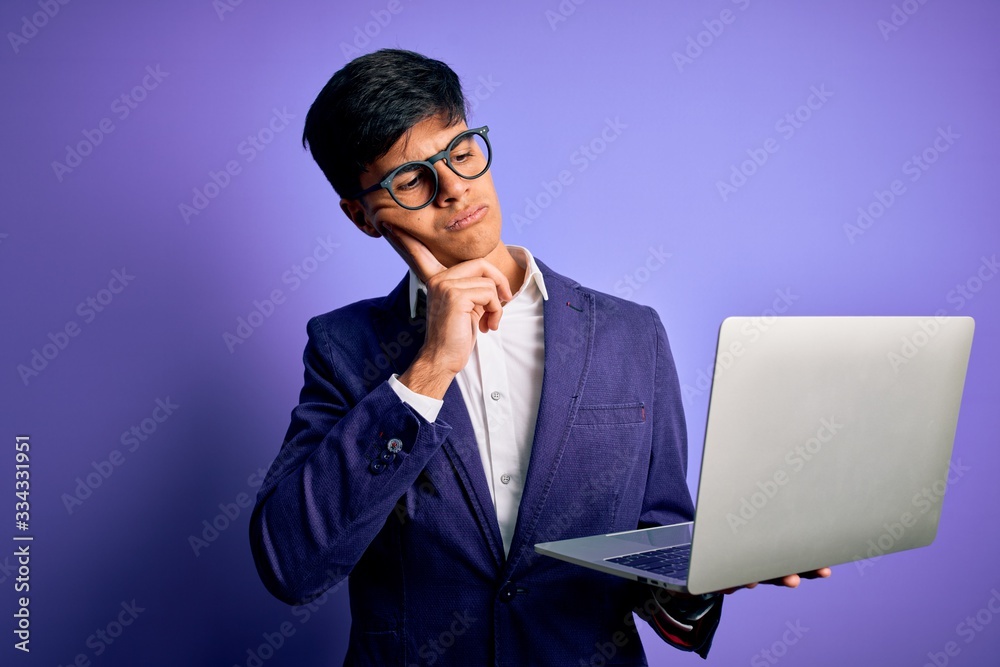 Young handsome business man wearing glasses working using laptop over purple background serious face thinking about question, very confused idea Young handsome business man wearing glasses working using laptop over purple background serious face thinking about question, very confused idea