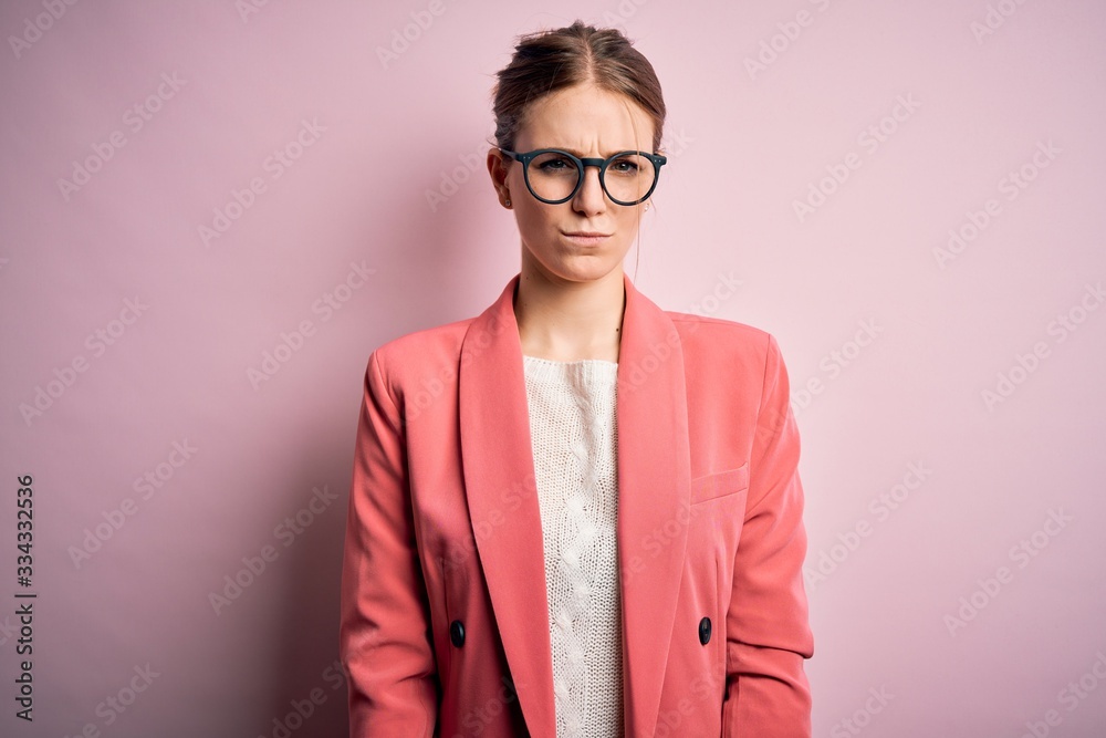 Young beautiful redhead woman wearing jacket and glasses over isolated pink background skeptic and nervous, frowning upset because of problem. Negative person.