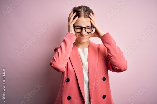 Young beautiful redhead woman wearing jacket and glasses over isolated pink background suffering from headache desperate and stressed because pain and migraine. Hands on head. © Krakenimages.com