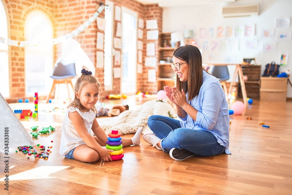 Caucasian girl kid playing and learning at playschool with female teacher. Mother and daughter at playroom playing with inteligence toys Caucasian girl kid playing and learning at playschool with female teacher. Mother and daughter at playroom playing with inteligence toys