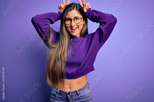 Young beautiful smart woman wearing glasses over purple isolated background Posing funny and crazy with fingers on head as bunny ears, smiling cheerful