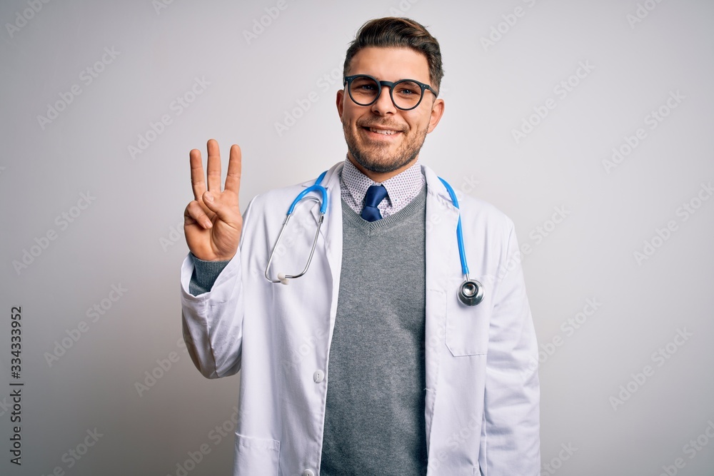 Young doctor man with blue eyes wearing medical coat and stethoscope over isolated background showing and pointing up with fingers number three while smiling confident and happy. Young doctor man with blue eyes wearing medical coat and stethoscope over isolated background showing and pointing up with fingers number three while smiling confident and happy.